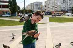 微笑可爱的高加索人青少年男孩表达积极的情绪喂养岩石鸽子城市广场