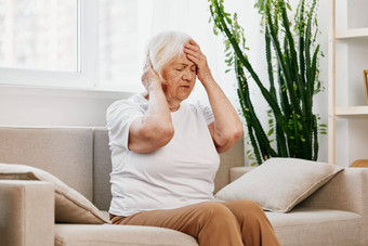 上了年纪的女人严重的疼痛头坐着沙发上健康问题年龄可怜的质量生活祖母灰色的头发持有头偏头痛高血压力