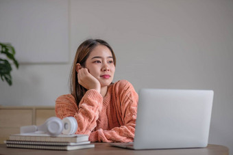 肖像微笑笑年轻的女人坐着表格穿无线耳机移动PC年轻的女看视频电影网络研讨会视频调用朋友家庭