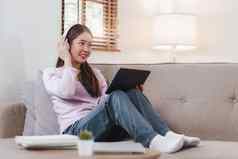 有吸引力的亚洲女人休息舒适的生活房间数字平板电脑放松沙发生活方式