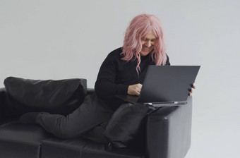 肖像男人。粉红色的假发坐着沙发打字移动PC