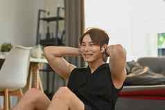 运动年轻的亚洲男人。坐联合包裹ABS锻炼首页健康的生活方式体育运动概念