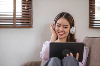 美丽的亚洲年轻的女人穿休闲坐沙发上电脑移动PC娱乐社会媒体放松微笑笑自由女人工作在线出售市场营销购物在线首页