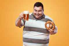 年轻的脂肪男人。啤酒节喝啤酒吃椒盐卷饼黄色的背景