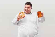 年轻的脂肪男人。啤酒节喝啤酒吃椒盐卷饼孤立的白色背景