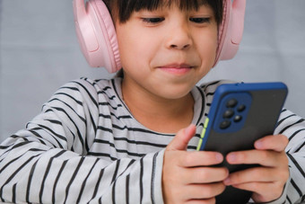 可爱的小学学校女孩穿耳机持有智能手机快乐亚洲女孩研究在线智能手机在家教育听音乐玩游戏