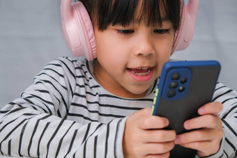 可爱的小学学校<strong>女孩</strong>穿耳机持有智能手机快乐亚洲<strong>女孩</strong>研究在线智能手机在家教育<strong>听音乐</strong>玩游戏