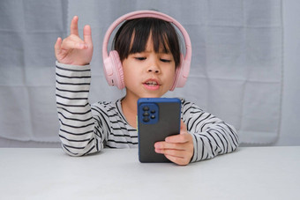 可爱的小学学校女孩穿耳机持有智能手机快乐亚洲女孩研究在线智能手机在家教育听音乐玩游戏