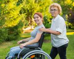 上了年纪的女人携带成人女儿坐着轮椅走在户外