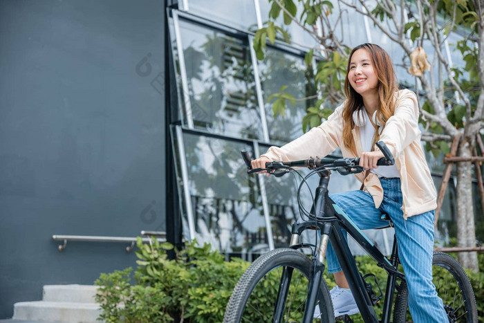 快乐亚洲美丽的年轻的女人骑自行车街户外建筑城市