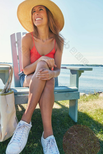浸泡太阳快乐的年轻的女人穿他坐着椅子湖太阳