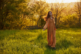 快乐的女人站绿色场微笑相机长橙色衣服照亮温暖的射线设置太阳
