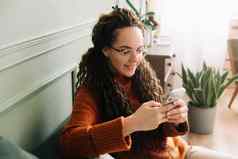 快乐年轻的女人智能手机在线购物沙发上首页放松夫人享受技术移动应用程序电子商务