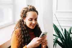 年轻的女人浏览在线手机坐着舒适快乐女人购物智能手机放松沙发上微笑夫人智能手机社会媒体电子商务