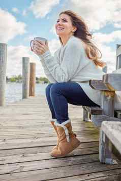秋天年可爱的微笑美丽的年轻的女人享受温暖的饮料放松板凳上湖