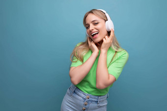 可爱的金发碧眼的女孩休闲装听音乐应用程序大白色耳机蓝色的背景