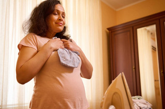 令人愉快的怀孕了女人大肚子持有熨紧身衣裤未来新生儿婴儿
