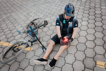 不开心骑自行车的人坐着人行道上膝盖疼痛概念骑自行车的人膝盖受伤在户外骑自行车的人膝盖疼痛在户外