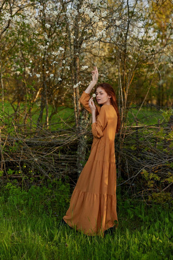 优雅的复杂的女人提出了站柳条栅栏别墅长橙色衣服提高手