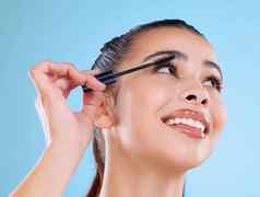 时间睫毛膏工作室拍摄有吸引力的年轻的女人应用睫毛膏蓝色的背景