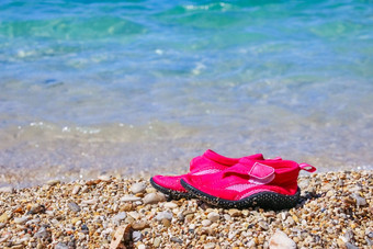 一对粉红色的游泳鞋子大理石卵石海滩绿松石海水夏天假期概念孩子们鞋子海滩游泳氯丁橡胶鞋子水鞋子岩石海滩