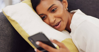 女孩沙发微笑打字电话生活房间社会媒体技术沟通快乐年轻的女人说谎沙发上聊天朋友在线看有趣的视频