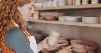 陶器女人艺术家架子上陶瓷杯商店检查质量有创意的类粘土模具车间爱好女企业家准备艺术项目出售启动