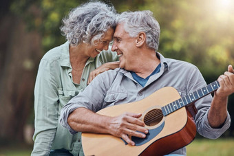 高级夫妇吉他爱公园玩浪漫的爱感情音乐首歌妻子浪漫退休高级男人。女人玩字符串仪器笑户外森林