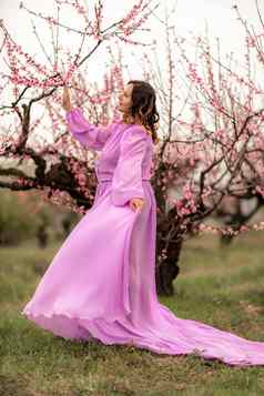 女人桃子开花快乐卷曲的女人粉红色的衣服走花园开花桃子树春天
