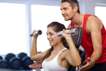 分享专业知识教练帮助年轻的女人重量训练健身房