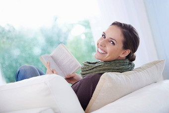 引人入胜的放松年轻的女人阅读引人入胜的沙发上