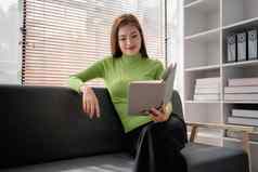 亚洲年轻的女人使笔记纸笔记本坐着舒适的沙发背景窗口漂亮的女写作笔记日记使列表放松首页