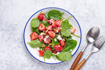 光健康的夏天沙拉新鲜的草莓菠菜奶油奶酪核桃白色陶瓷板白色乡村石头背景