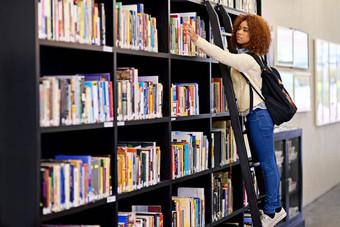 达到知识年轻的女人达到书书架上大学图书馆