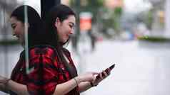 年轻的亚洲女人智能手机站购物区城市
