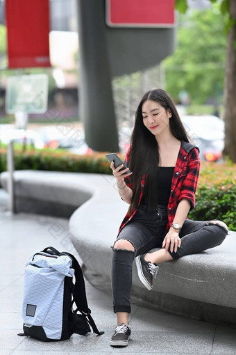 完整的长度肖像亚洲女人坐着在户外城市聪明的电话
