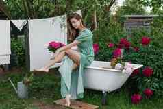女人坐着铸铁浴缸院子里国家房子布什开花牡丹概念夏天国家生活浴室街盛开的花园国家