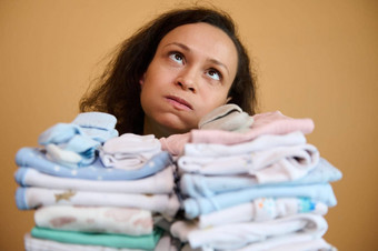 头像年轻的妈妈。持有堆栈洗熨婴儿衣服叹息累了家庭家务