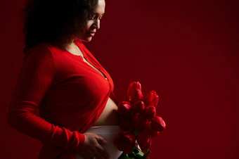 裁剪视图怀孕了女人准妈妈。触碰肚子摆姿势红色的郁金香孤立的红色的背景