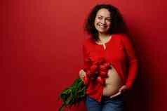令人愉快的少数民族怀孕了女人持有红色的郁金香触碰肚子神秘的微笑红色的背景