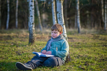 英俊的男孩围巾春天公园坐着桦木树阅读书享受梦想