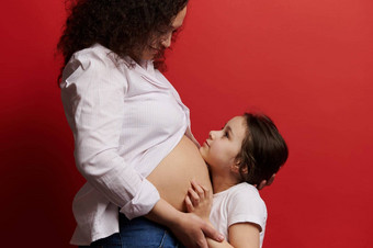 快乐女孩拥抱肚子怀孕了妈妈孤立的红色的颜色背景快乐母亲的一天怀孕
