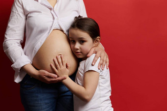 特写镜头怀孕了妈妈。轻轻拥抱女儿触碰只肚子孤立的红色的背景