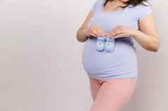 特写镜头怀孕了女人持有蓝色的针织婴儿靴袜子肚子孤立的白色背景分娩