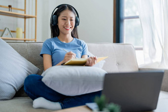 年轻的亚洲女人听音乐耳机写作请注意书工作的想法日记放松概念