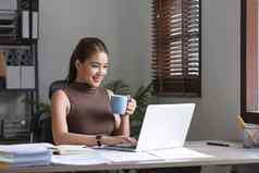 快乐亚洲女商人工作检查工作移动PC电脑舒适的杯咖啡办公室