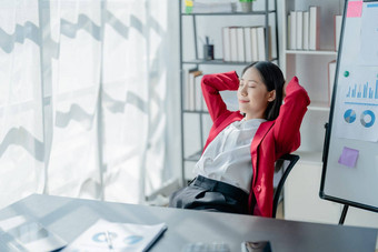 后视图年轻的女商人倾斜回来舒适的椅子坐着现代办公室成功的女人员工规划未来可视化思考项目策略