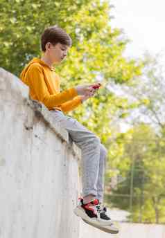 深思熟虑的少年男孩休息持有智能手机网络阳光明媚的一天在户外