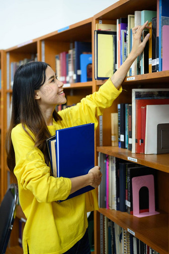 快乐的学生女人采取教科书架子上研究图书馆教育学习青年生活方式概念