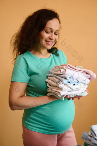 快乐怀孕了女人准备工作出生孩子持有新生儿衣服站熨衣服董事会